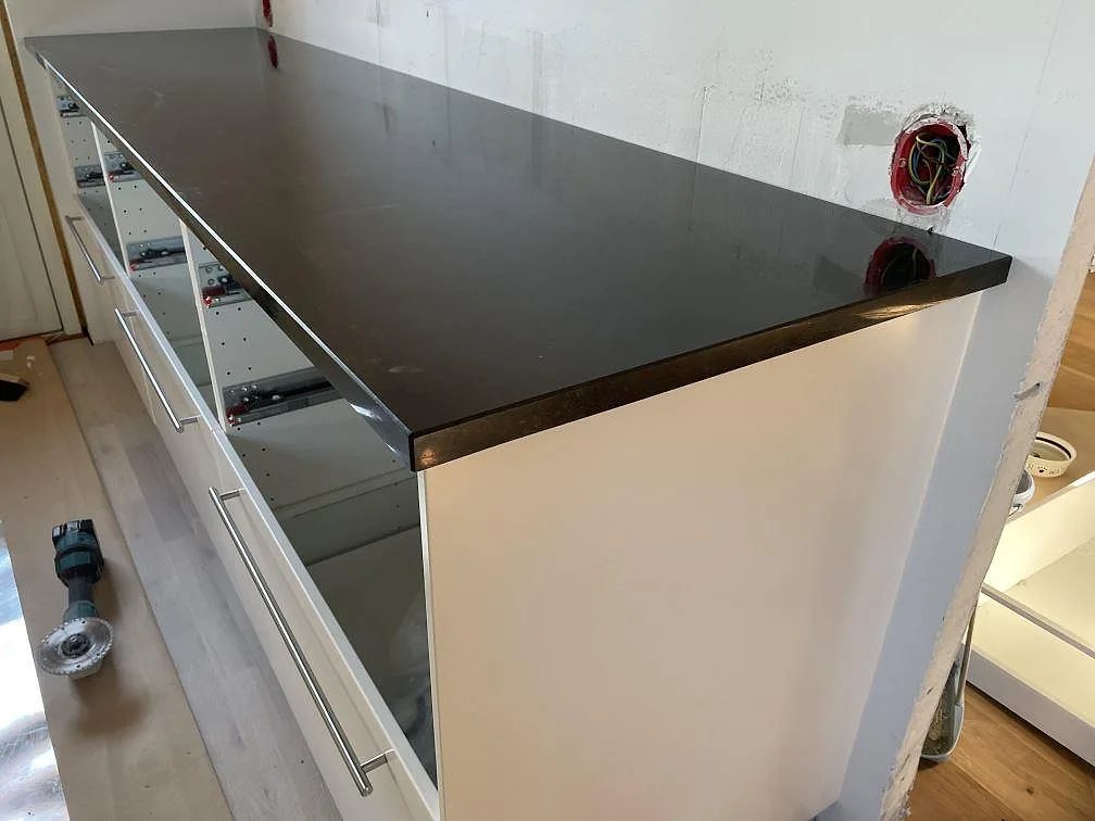 Lång polerad bänkskiva i Nero Assoluto granit över vita köksstommar med handtag under montering i Malmö.