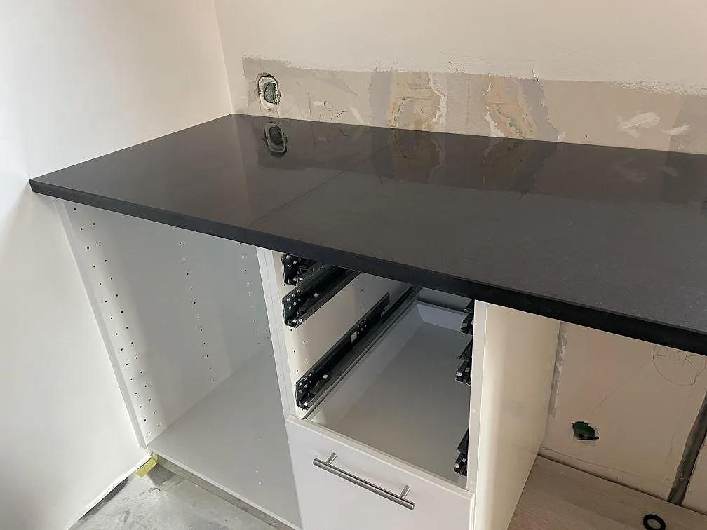 Hörndel av polerad Nero Assoluto granit i ett kök med vita skåpstommar och oinredd väggyta i Malmö.