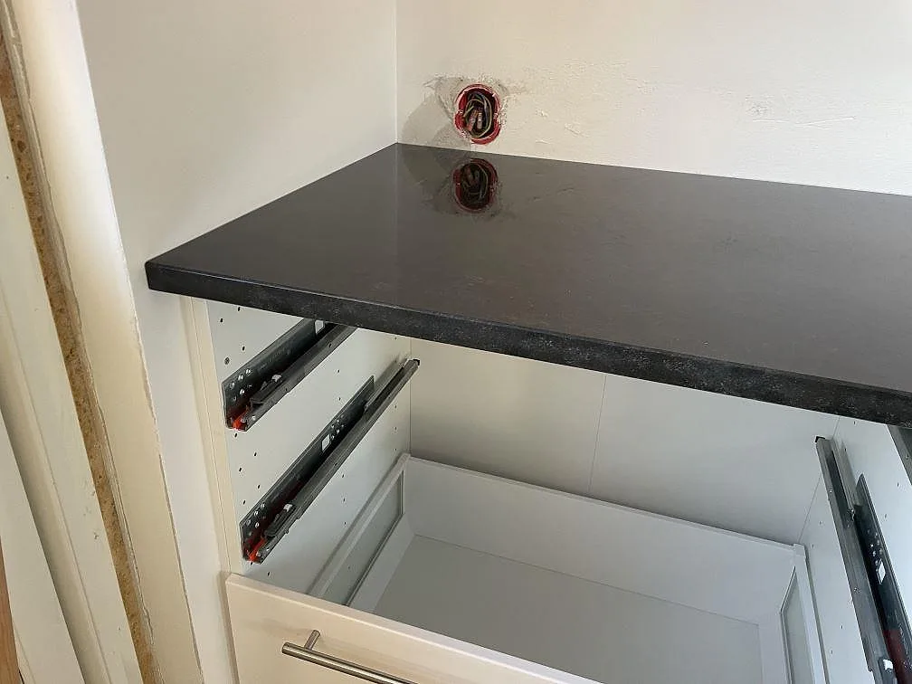 Detalj av polerad Nero Assoluto granit över vit köksstomme med utdragen låda under montering i Malmö.