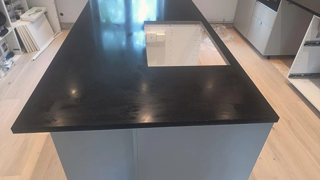 Närbild av matt Nero Assoluto granit på köksö med stor rektangulär öppning och vit skåpsinredning i Malmö.