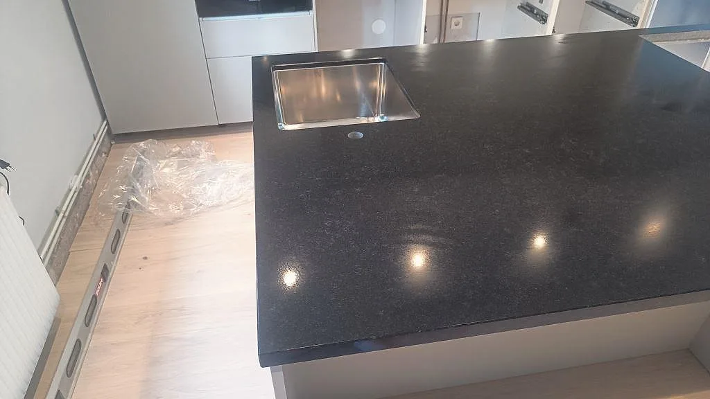 Detalj vid diskhon i matt Nero Assoluto granit med underlimmad rostfri diskho och ljusa trägolv i Malmö.
