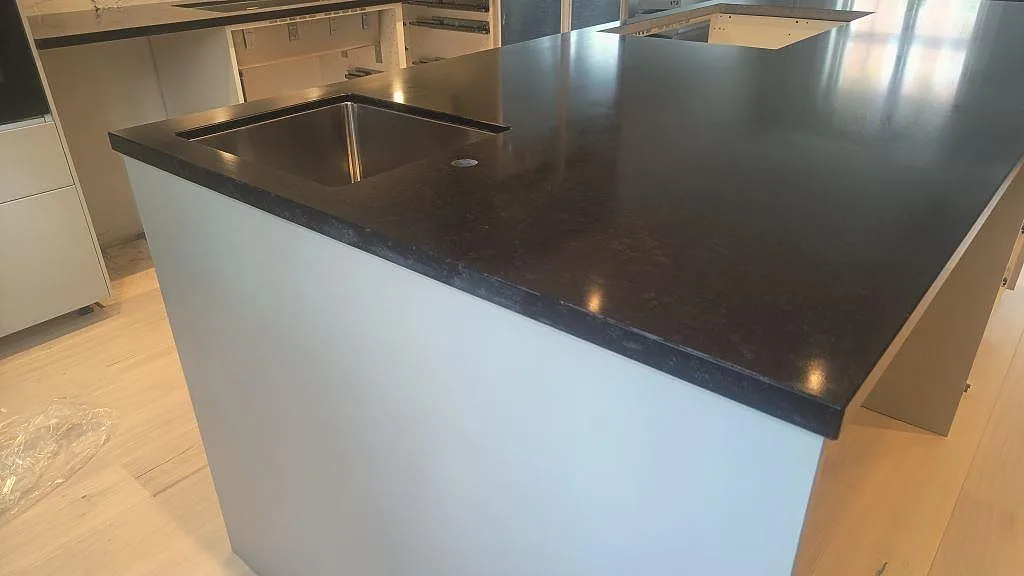 Matt köksö i Nero Assoluto granit med underlimmad rostfri diskho och mörk bänkyta i ett kök i Malmö.