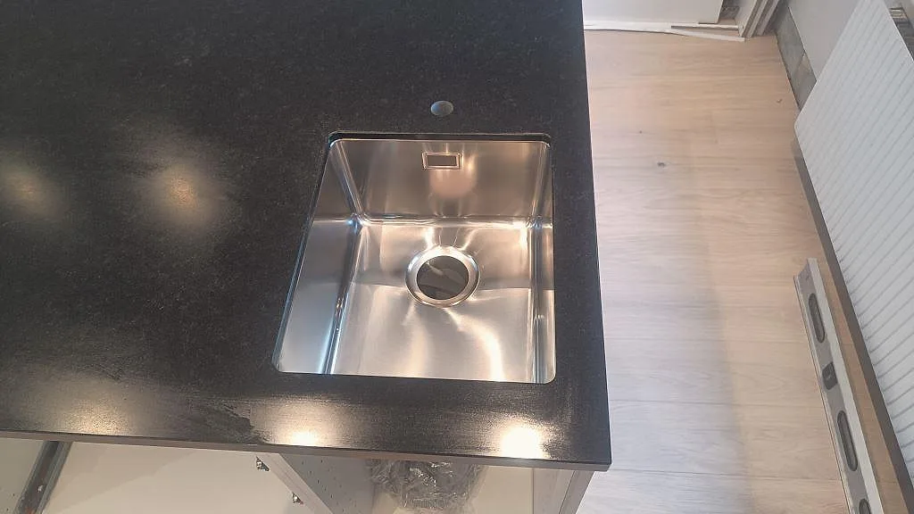 Närbild av underlimmad rostfri diskho i matt Nero Assoluto granit på köksö i Malmö.