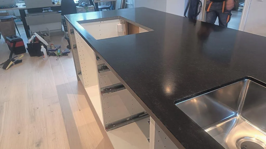 Stor köksö i matt Nero Assoluto granit med diskho, öppning i skivan och monteringsverktyg i ett kök i Malmö.