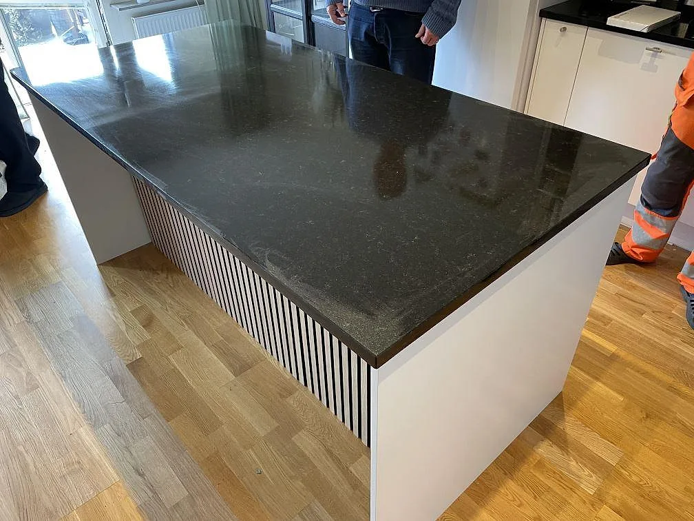 Stor köksö med bänkskiva i polerad Nero Assoluto granit på vit ribbad bas i ett kök i Malmö.