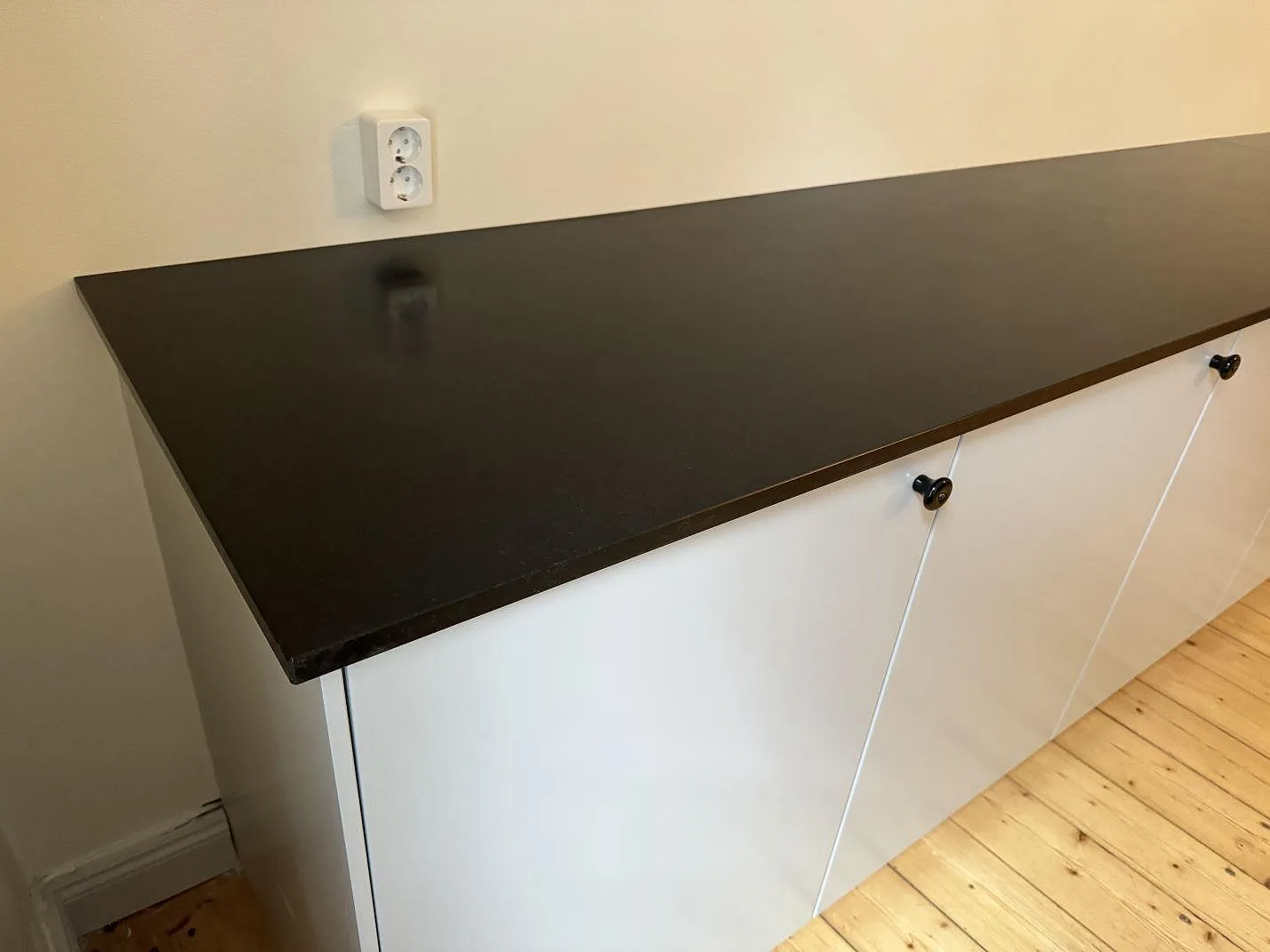 Matt svart Nero Assoluto granitskiva med vit köksinredning och trägolv i Malmö.