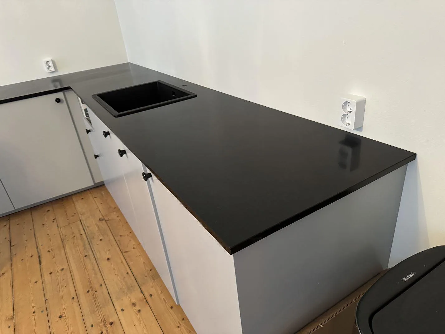 L-formad köksbänkskiva i matt Nero Assoluto granit med svart diskho ovanpå stenen i ett kök i Malmö.