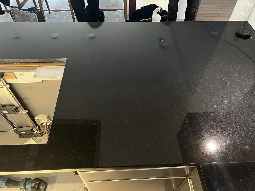 Närbild på blank svart Nero Assoluto granit med speglingar i en polerad köksbänkskiva i Malmö.