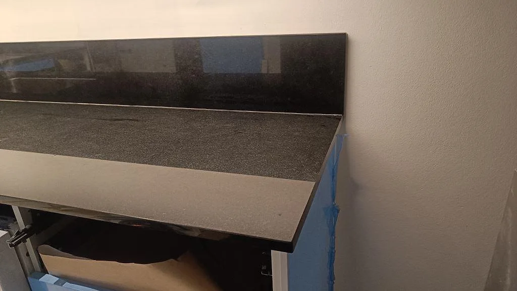 Höger bänkrad i polerad Nero Assoluto-granit med blankt svart stänkskydd över blå underskåp i Malmö.