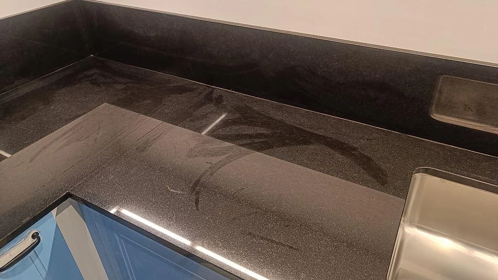 L-format hörn i polerad Nero Assoluto-granit med blå köksluckor, rostfri diskho och svart stänkskydd i Malmö.