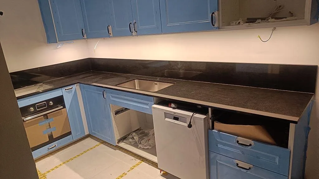 Köksbänkskiva i polerad Nero Assoluto-granit med underlimmad rostfri diskho, hällurtag, diskmaskin och blå luckor i Malmö.