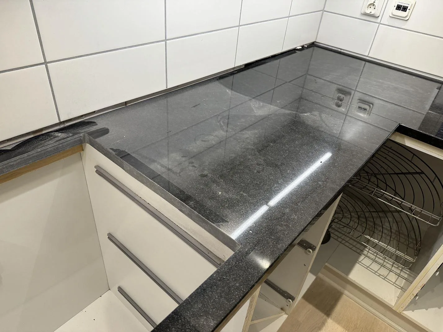 L-formad köksbänkskiva i polerad Nero Assoluto granit med svart stenyta och vit kakelvägg i ett kök i Malmö.