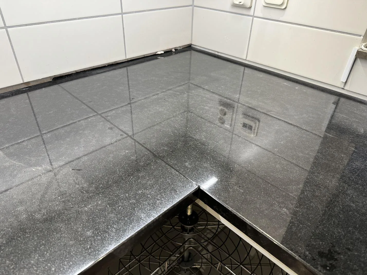 Närbild på blankpolerad Nero Assoluto granit med L-format hörn och vit kakelvägg i Malmö.
