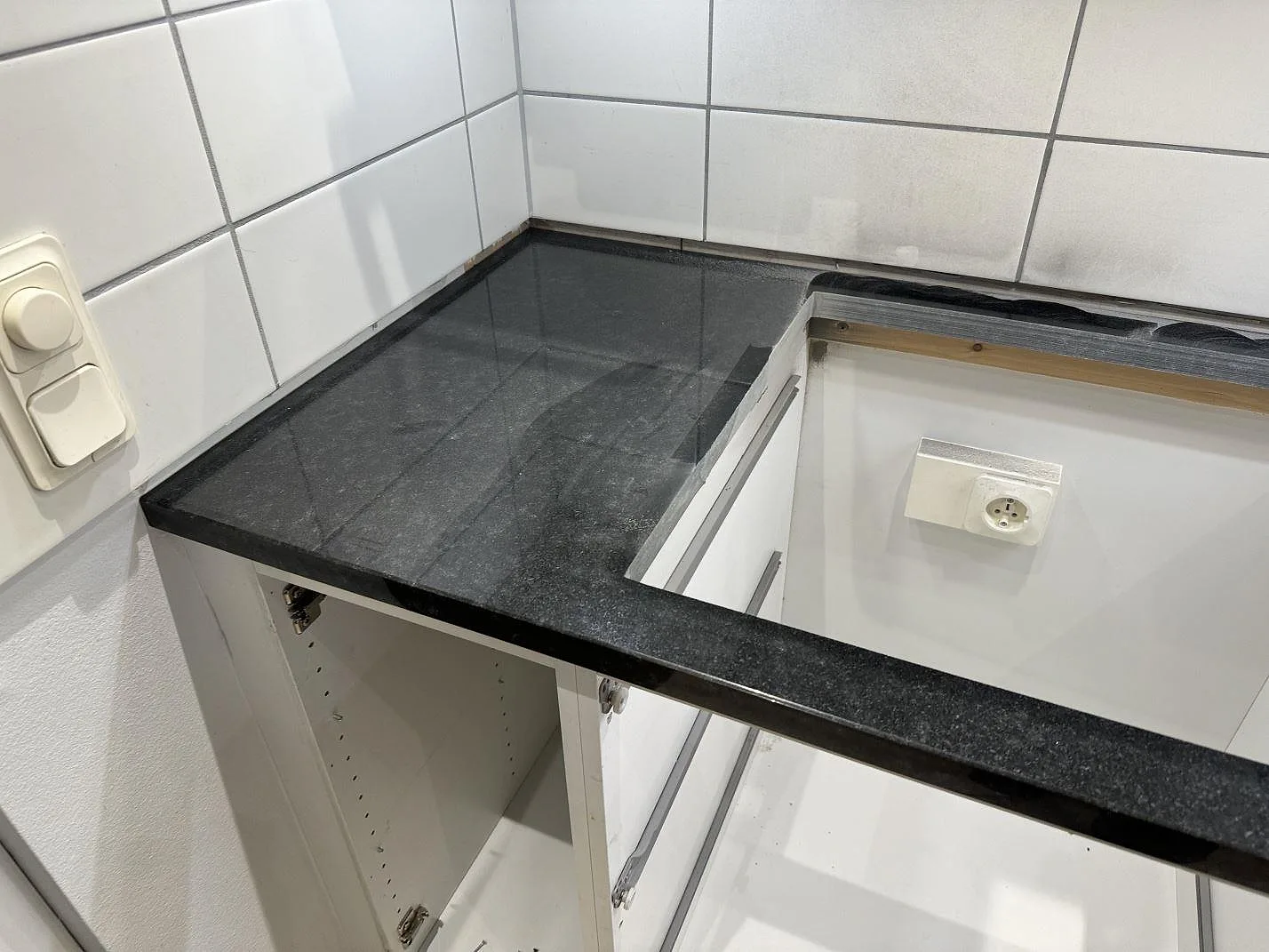 Installerad Nero Assoluto köksbänkskiva i polerad svart granit med vit kakelvägg och öppna stommar i Malmö.