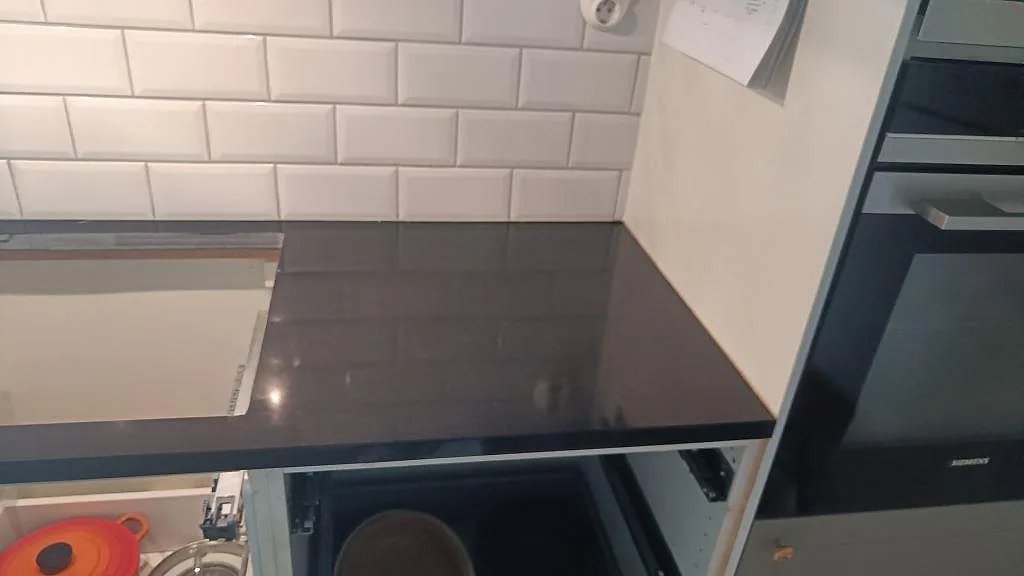 Hällsida med matt Nero Assoluto granit, vit kakelvägg och ugnsskåp under montering i Malmö.