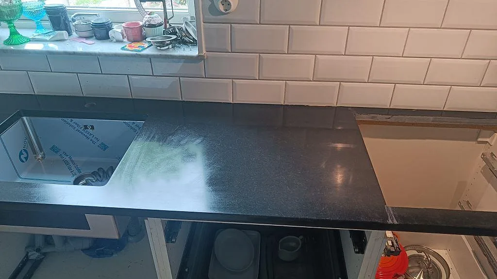 Installerad köksbänkskiva i matt Nero Assoluto granit med diskhoöppning och hällurtag under montering i Malmö.