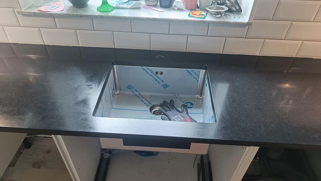 Närbild på matt Nero Assoluto granit vid diskhourgat och vit kakelvägg i ett kök i Malmö.