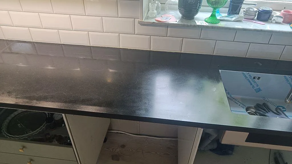 Rak bänkskiveyta i matt Nero Assoluto granit med del av diskhoöppning i ett kök i Malmö.