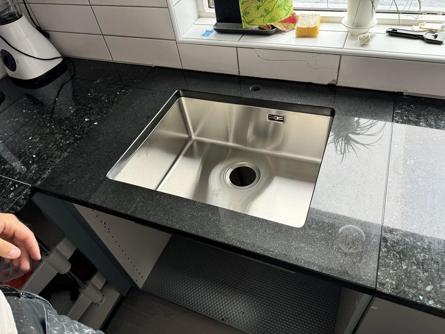Köksbänkskiva i polerad Nero Assoluto granit med rostfri diskho och blank mörk yta i ett kök i Malmö.
