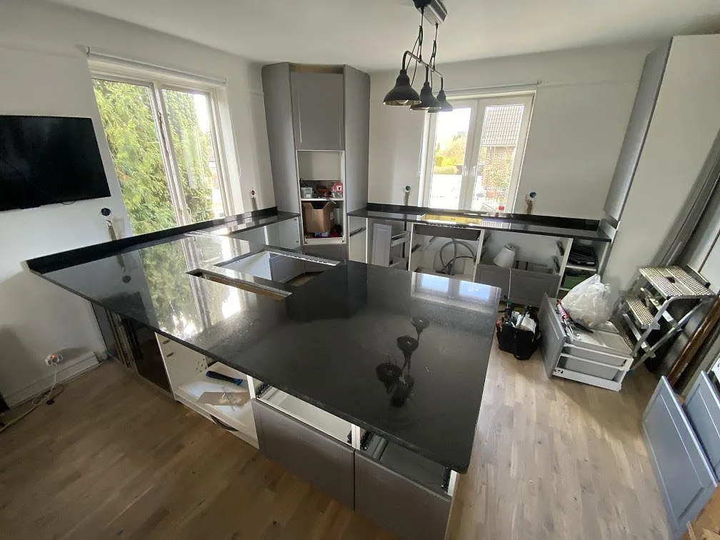Köksbänkskiva och köksö i polerad Nero Assoluto granit med låg stänkkant i ett kök under montering i Malmö.