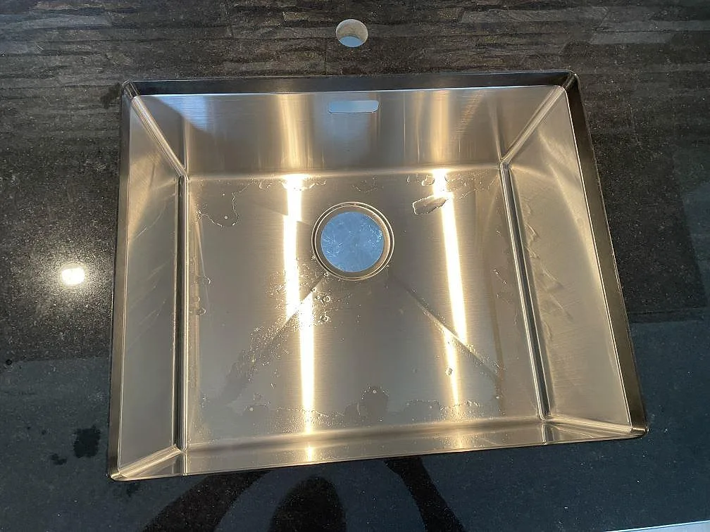 Närbild på underlimmad rostfri diskho i polerad Nero Assoluto granit i köket i Mellerud.