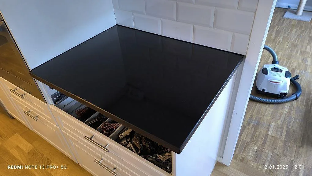 Detalj av polerad svart Nero Assoluto granit som köksbänkskiva vid vita luckor och vit kakelvägg i Motala.