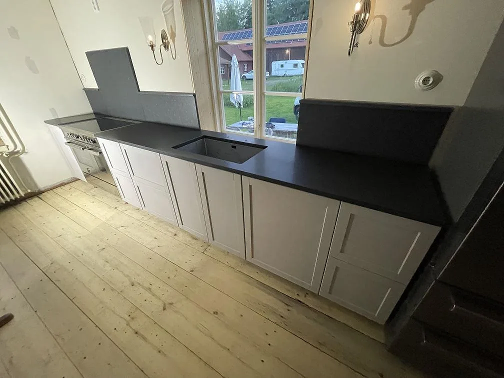 Köksbänkskiva i svart granit Nero Assoluto, matt, med uppvikt stänkskydd längs väggen i ett kök i Norberg.