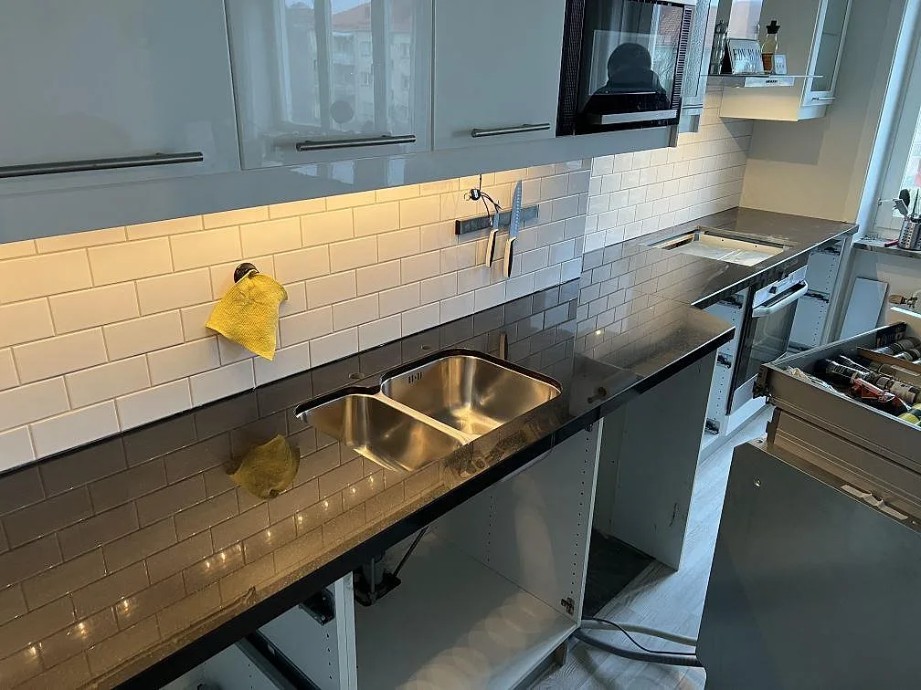 Lång köksbänkskiva i polerad Nero Assoluto granit med rostfri dubbelho och öppna underskåp i Norrköping.