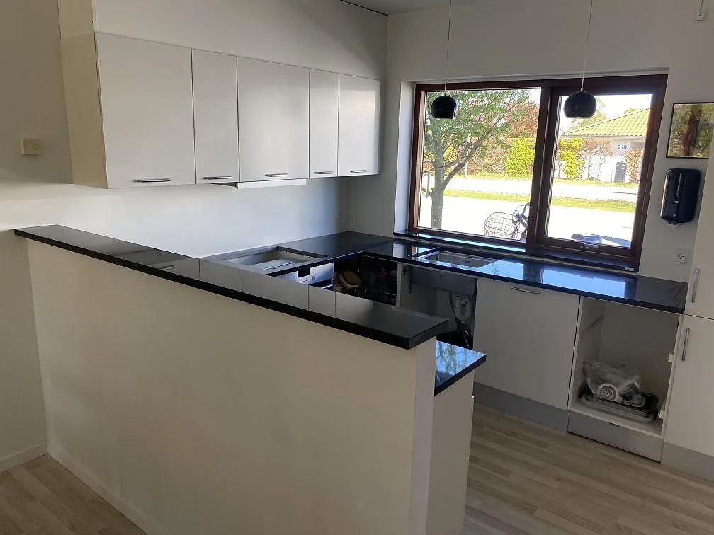 Köksbänkskivor i polerad Nero Assoluto, svart granit, längs ett ljust kök under montering i Roskilde.