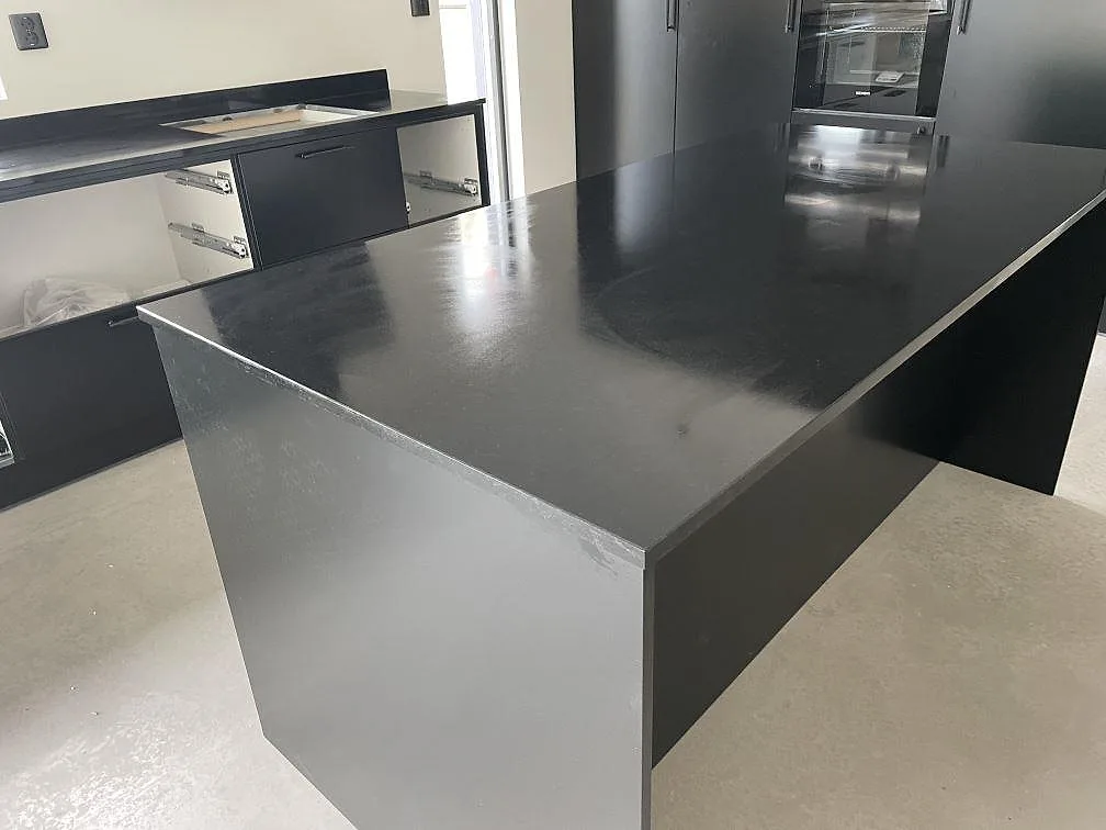 Närbild på stor köksö i matt Nero Assoluto-granit med mörka högskåp och väggbänk i bakgrunden i Säve.