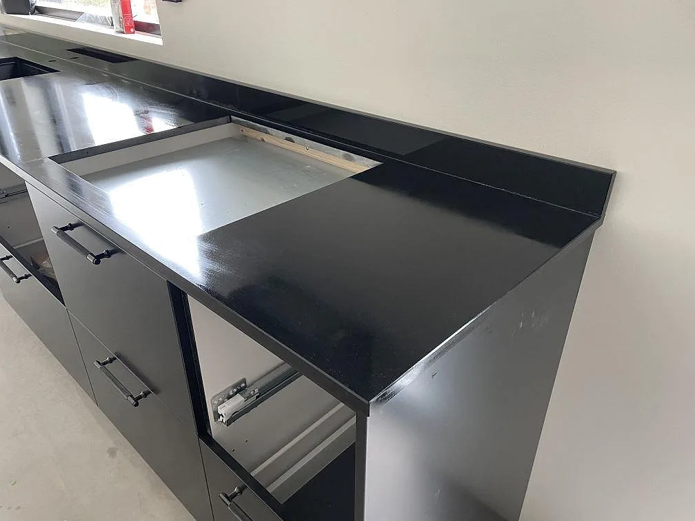 Detalj av väggbänk i matt Nero Assoluto-granit med uppvikt stänkkant och förberett urtag under fönster i Säve.