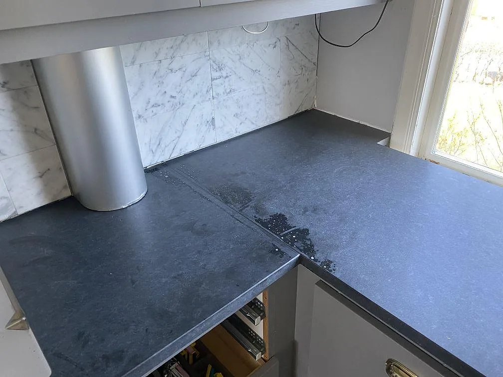 Hörn av matt Nero Assoluto-bänkskiva i granit mot vitt marmorkakel och rostfri köksfläkt i Sävedalen.