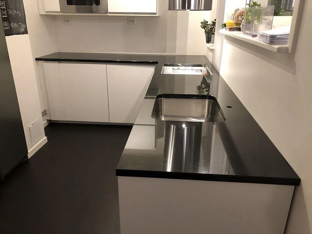 Köksbänkskiva i svart Nero Assoluto granit, polerad, i ett U-format vitt kök i Skövde med underlimmad rostfri diskho och håltagning för häll.