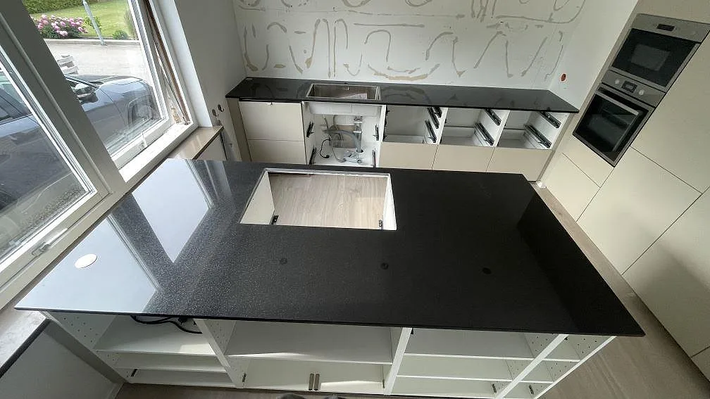 Köksbänkskiva i svart granit Nero Assoluto, polerad, med köksö, hällurtag och bakre bänk med rostfri diskho i ett kök i Skurup.