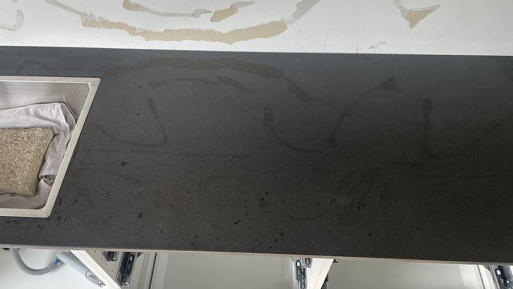 Detalj av polerad Nero Assoluto bänkskiva med diskho till vänster och mörk arbetsyta längs köksväggen i Skurup.