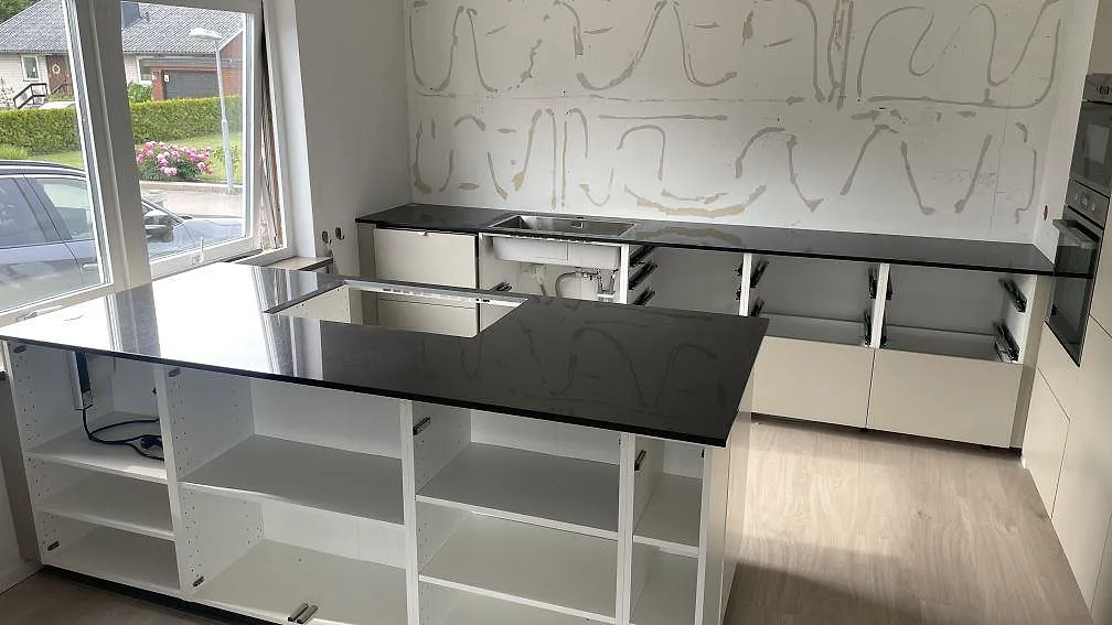 Polerad köksbänkskiva i Nero Assoluto med blank köksö och lång bakre bänk i ett kök under montering i Skurup.