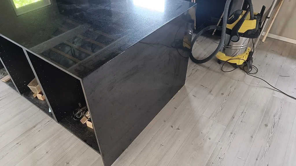 Detalj av polerad Nero Assoluto granit på köksö med mörk sidobeklädnad och öppen stomme i Staffanstorp.