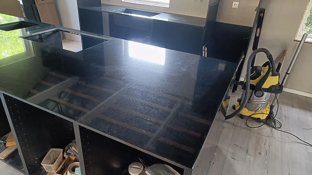 Blank köksö i Nero Assoluto granit, polerad, med öppna köksstommar under montering i Staffanstorp.