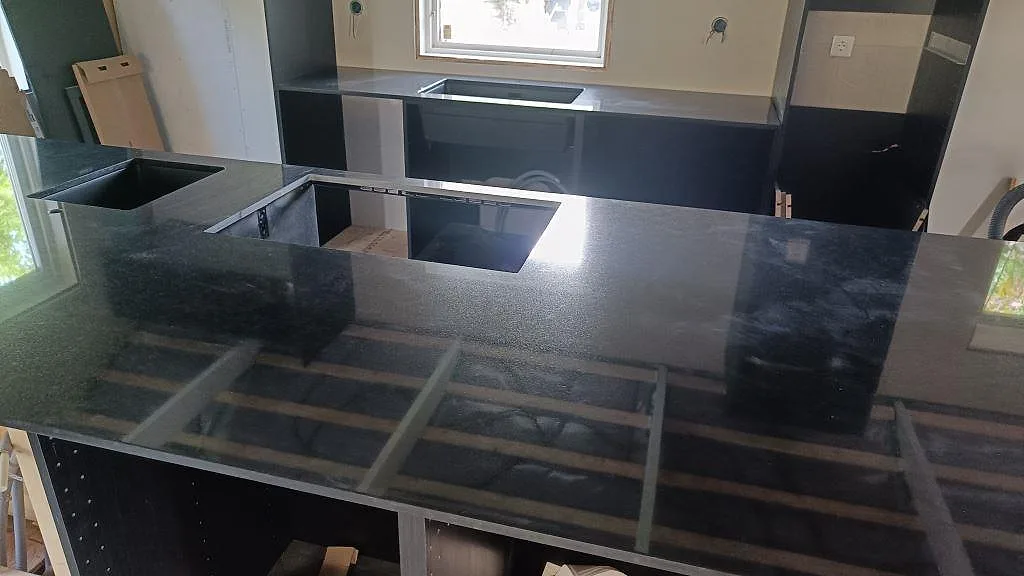 Köksbänkskiva i polerad Nero Assoluto granit med flera urtag och väggbänk under fönster i Staffanstorp.