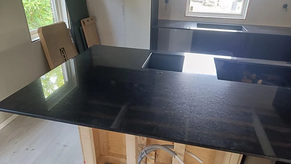 Polerad Nero Assoluto granit på köksö med rektangulärt urtag och matchande väggbänk i Staffanstorp.