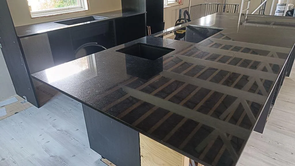 Polerad köksö i Nero Assoluto granit med svart diskho och reflekterande yta i ett kök i Staffanstorp.