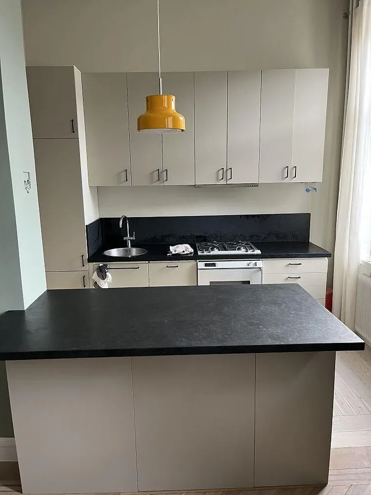 Köksbänkskiva i Nero Assoluto granit med mörk halvö, vask och spis i ett ljust kök i Stockholm.