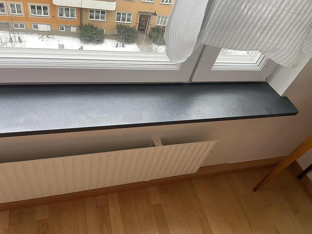 Lång fönsterbänk i granit Nero Assoluto med matt finish sedd längs hela skivan mot fönstret, Stockholm.