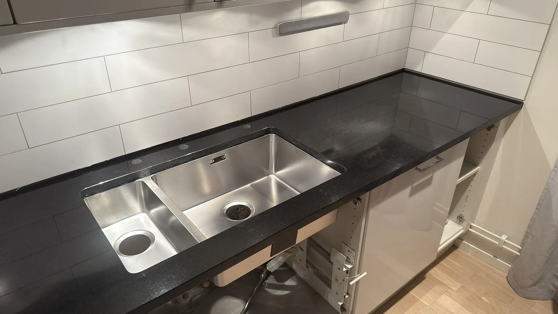 Närbild på underlimmad rostfri dubbeldiskho i polerad Nero Assoluto granitbänkskiva i ett kök i Stockholm.