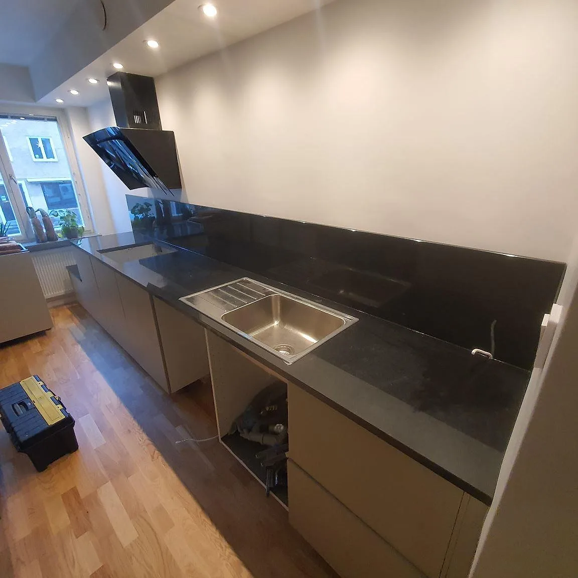 Köksbänkskiva i polerad svart Nero Assoluto-granit med uppvikt stänkskydd, underlimmad rostfri diskho och infälld häll i ett kök under montering i Sundbyberg.