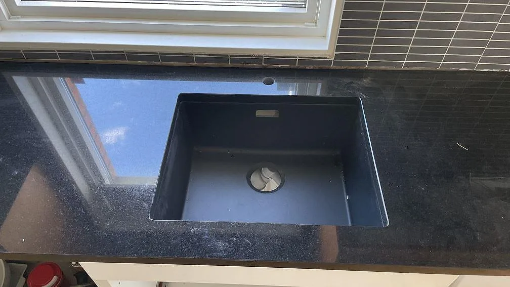 Svart diskho i polerad Nero Assoluto granit på en köksbänkskiva vid fönster i Svedala.
