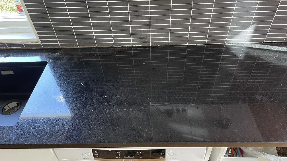 Lång arbetsyta i polerad Nero Assoluto granit med speglingar från mörkt kakel i kök i Svedala.
