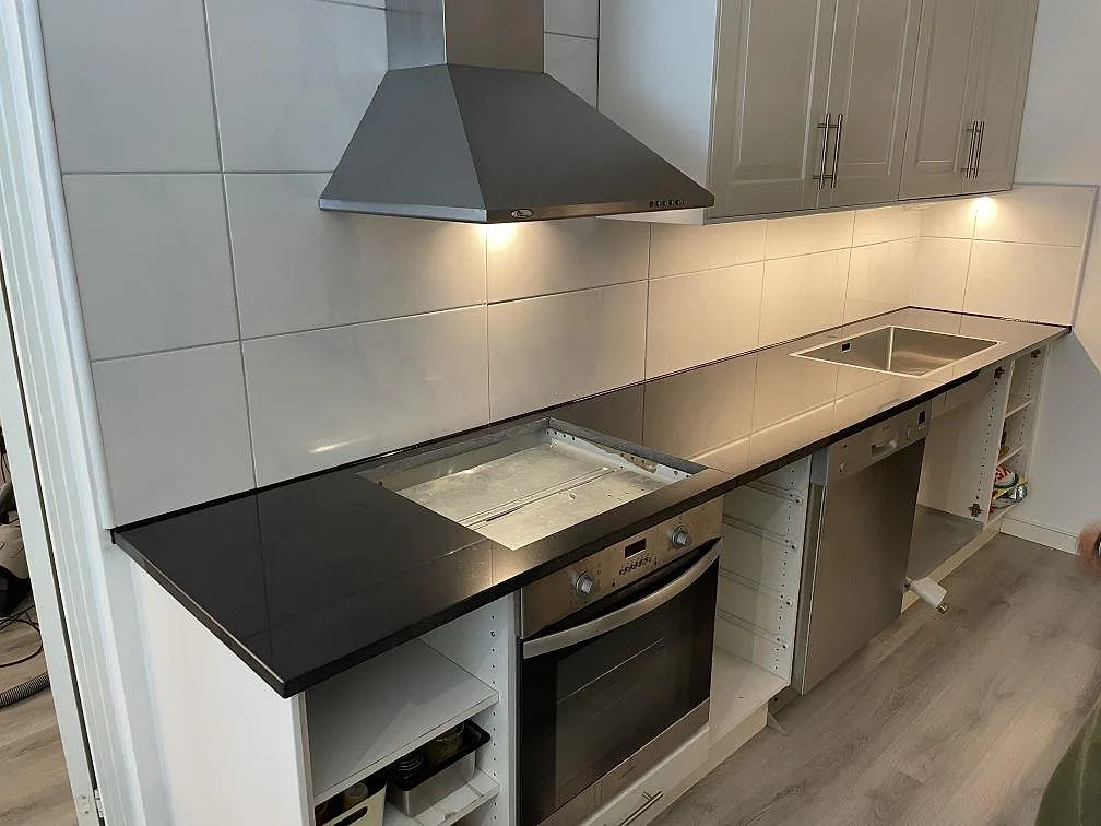 Rak köksbänkskiva i 30 mm polerad Nero Assoluto granit längs vit kakelvägg i ett kök i Täby.