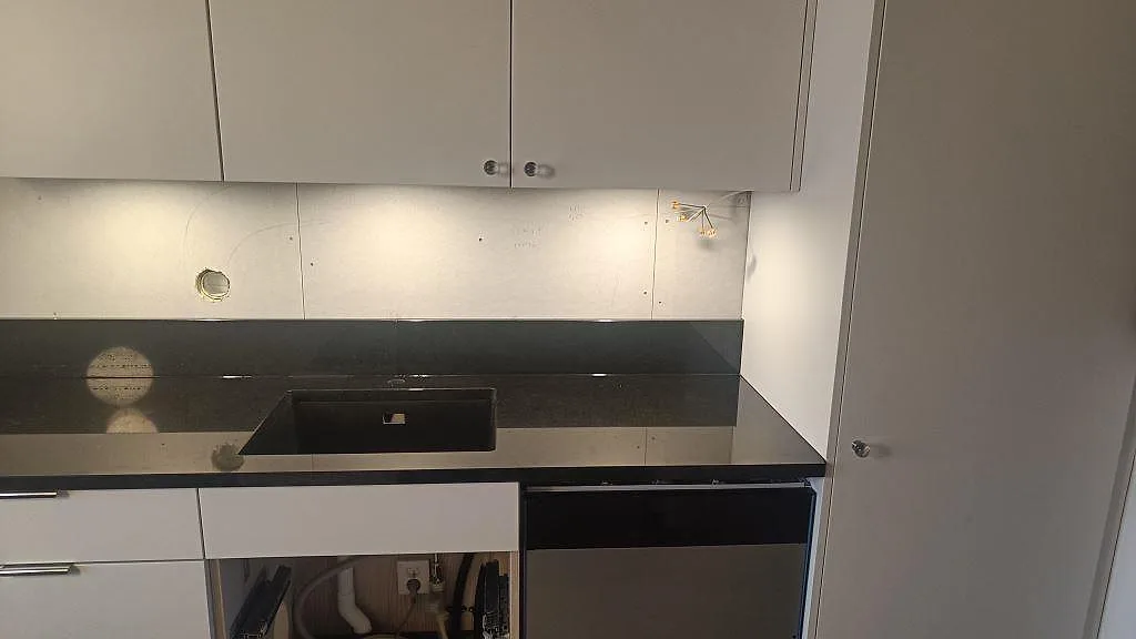 Köksbänkskiva i polerad svart granit Nero Assoluto med diskho, stänkkant och ljusa skåp under montering i Tibro.