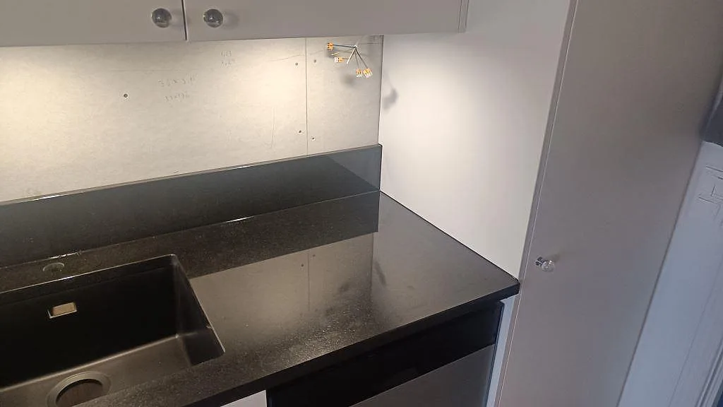 Detalj av polerad Nero Assoluto granit vid diskho och hörnyta med låg stänkkant i köket i Tibro.